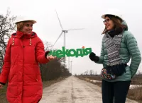 Zwei Frauen halten den Namen ihrer NGO vor Windrädern in der Ukraine hoch