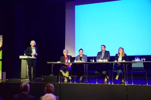 Vier Personen sitzen auf einem Podium und eine Frau moderiert eine Diskussion