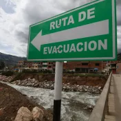 Schild mit der Aufschrift "Ruta de Evacuación" vor einem reißenden Bach