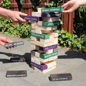 Hände, die einen Jenga-Turm bauen, dessen Steine mit Schlüsselwörtern aus der Bildungsarbeit versehen sind